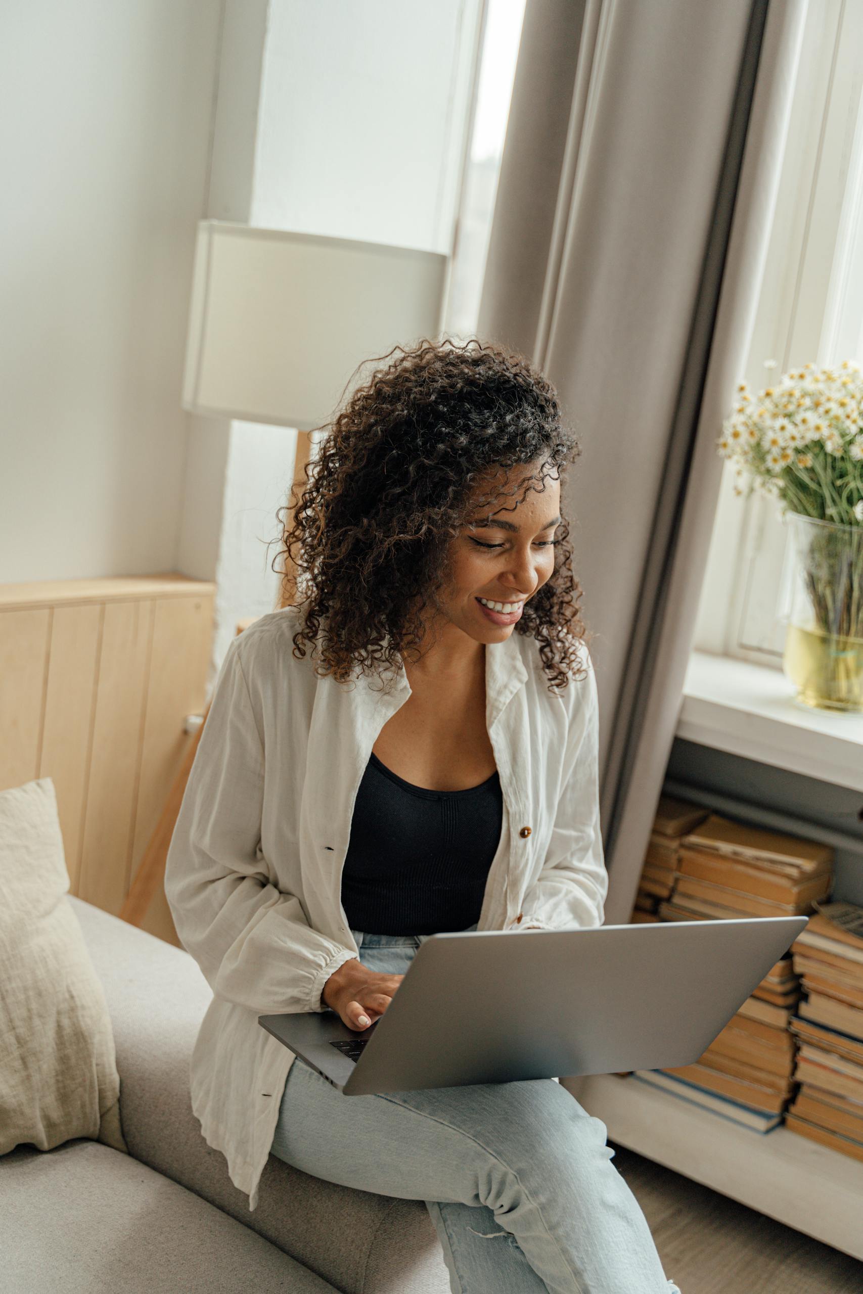 African American woman smiling while working on a laptop indoors, emphasizing freelance and remote work lifestyle.