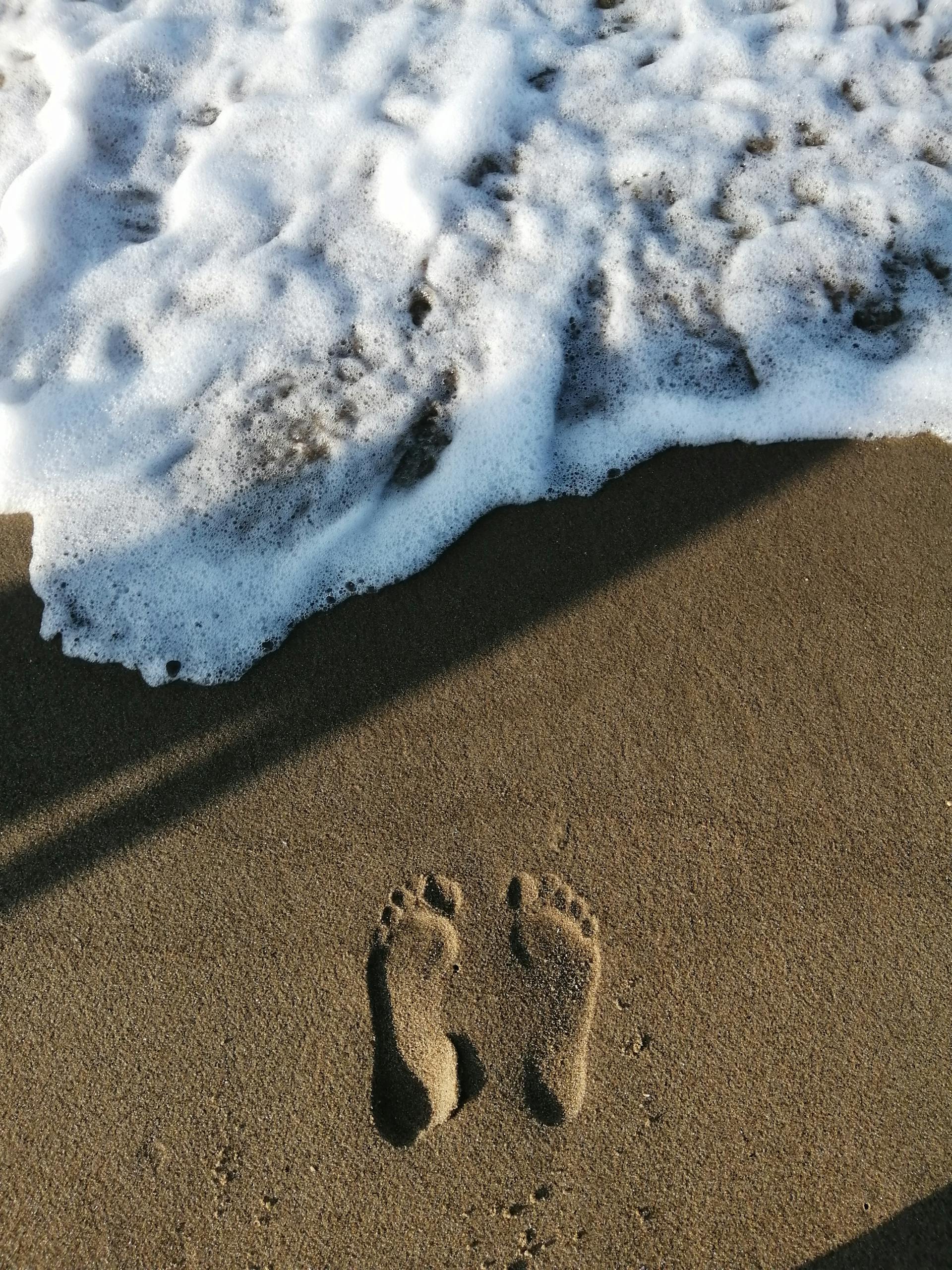 Footprints on a sandy beach with waves approaching, captured from above.